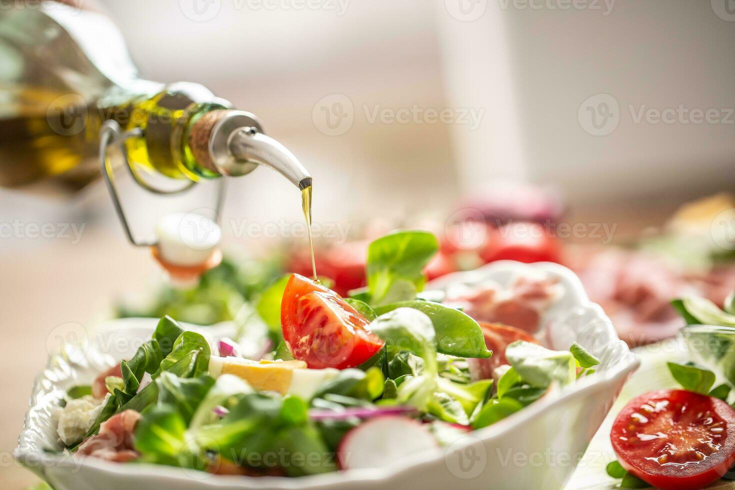Bottle with olive oil pouring into salad photo