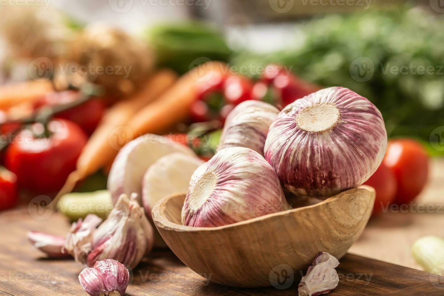 Garlic heads in wooden bowl surrounded by vegetables photo