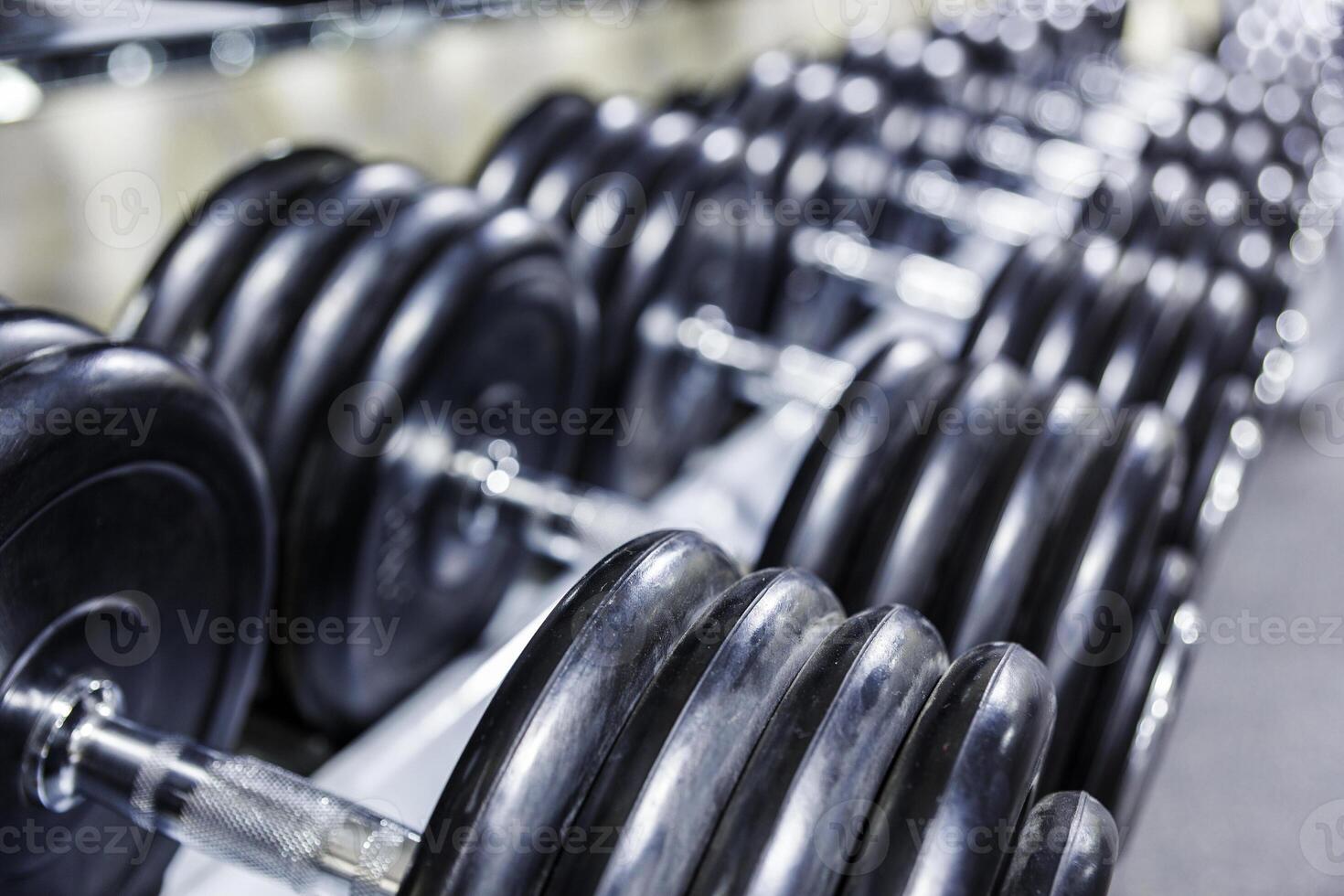 Black dumbbell set. Close up many rubberized dumbbells on rack in sport fitness center , Weight Training Equipment concept photo