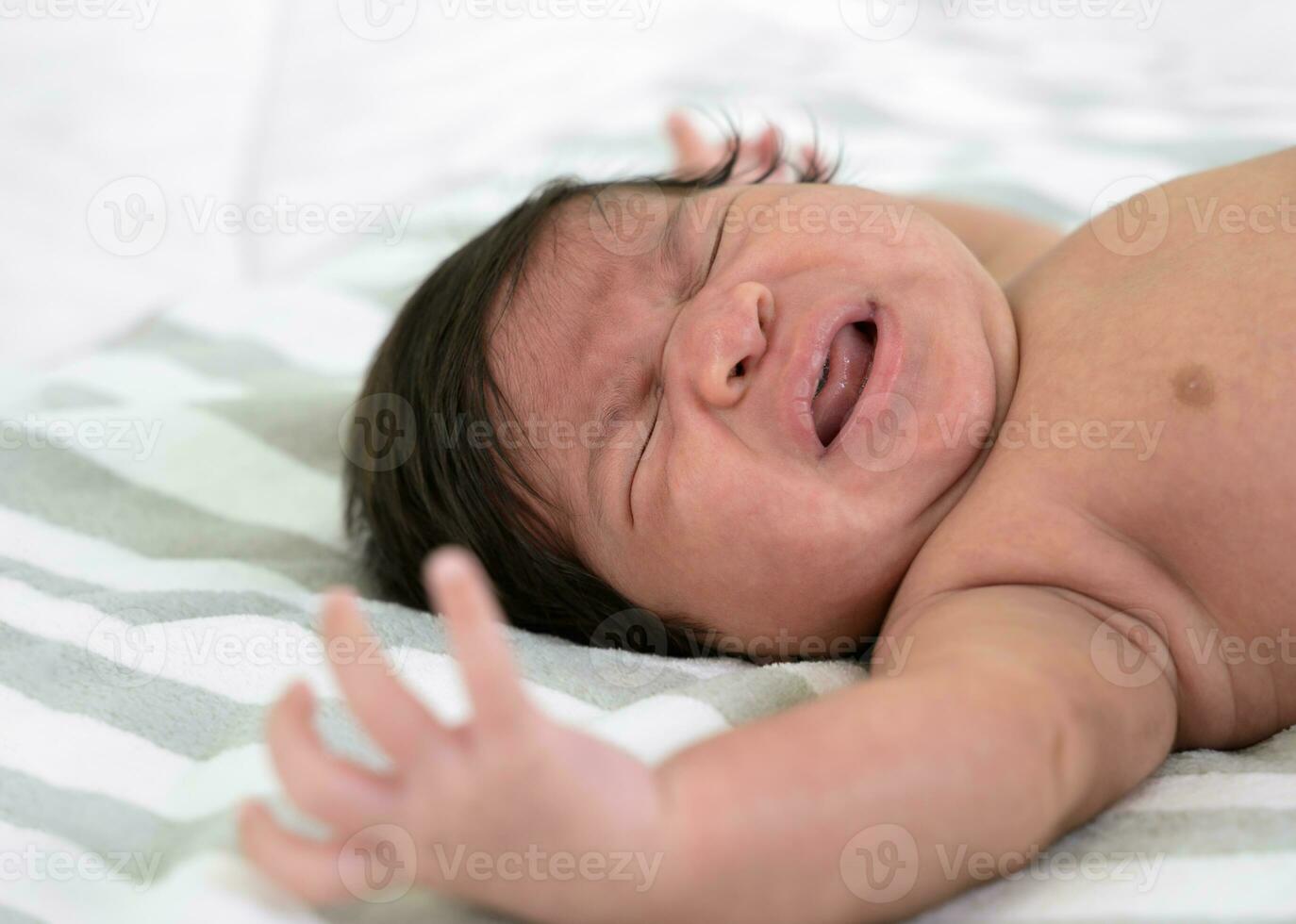 Crying newborn baby girl or boy lying on bed. photo