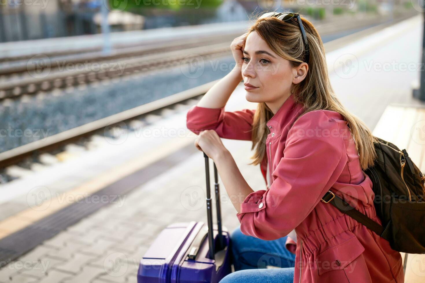 Adult woman is sitting at railway station and waiting for arrival of train. photo