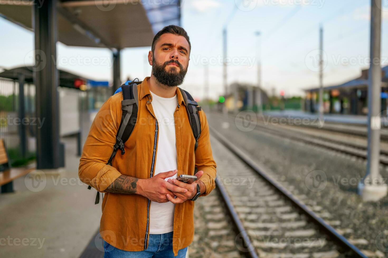 Adult man is standing at railway station and waiting for arrival of train. photo