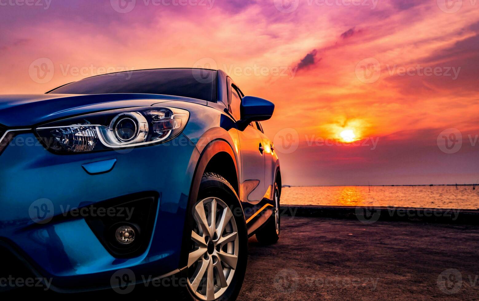 Blue compact SUV car with sport and modern design parked on concrete road by the sea at sunset. Environmentally friendly technology. Business success concept. photo