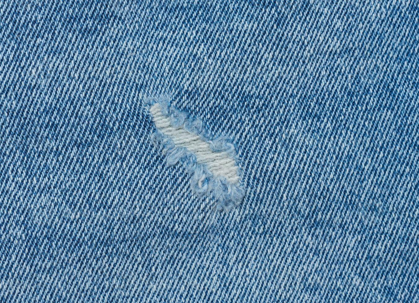 Fragment of blue jeans fabric with a hole, full frame, close up photo