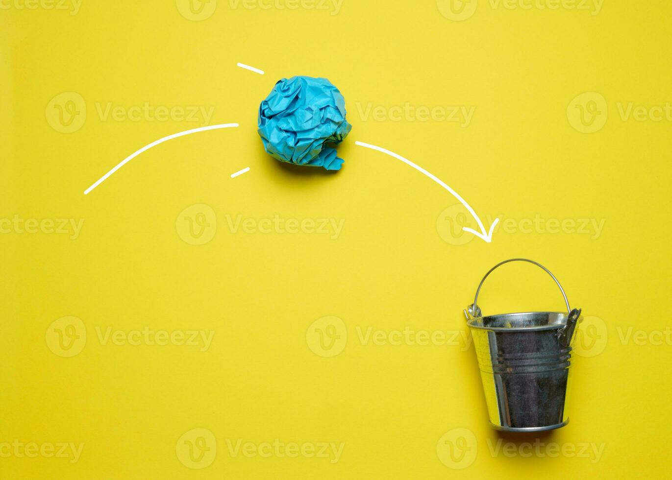 un estropeado papel pelota volador dentro un miniatura metal Cubeta en un amarillo fondo, concepto de buscando para nuevo ideas foto