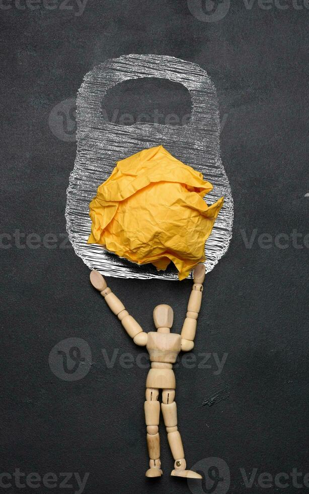 A wooden puppet toy holds a weight drawn on a chalkboard. The concept of a strong personality photo