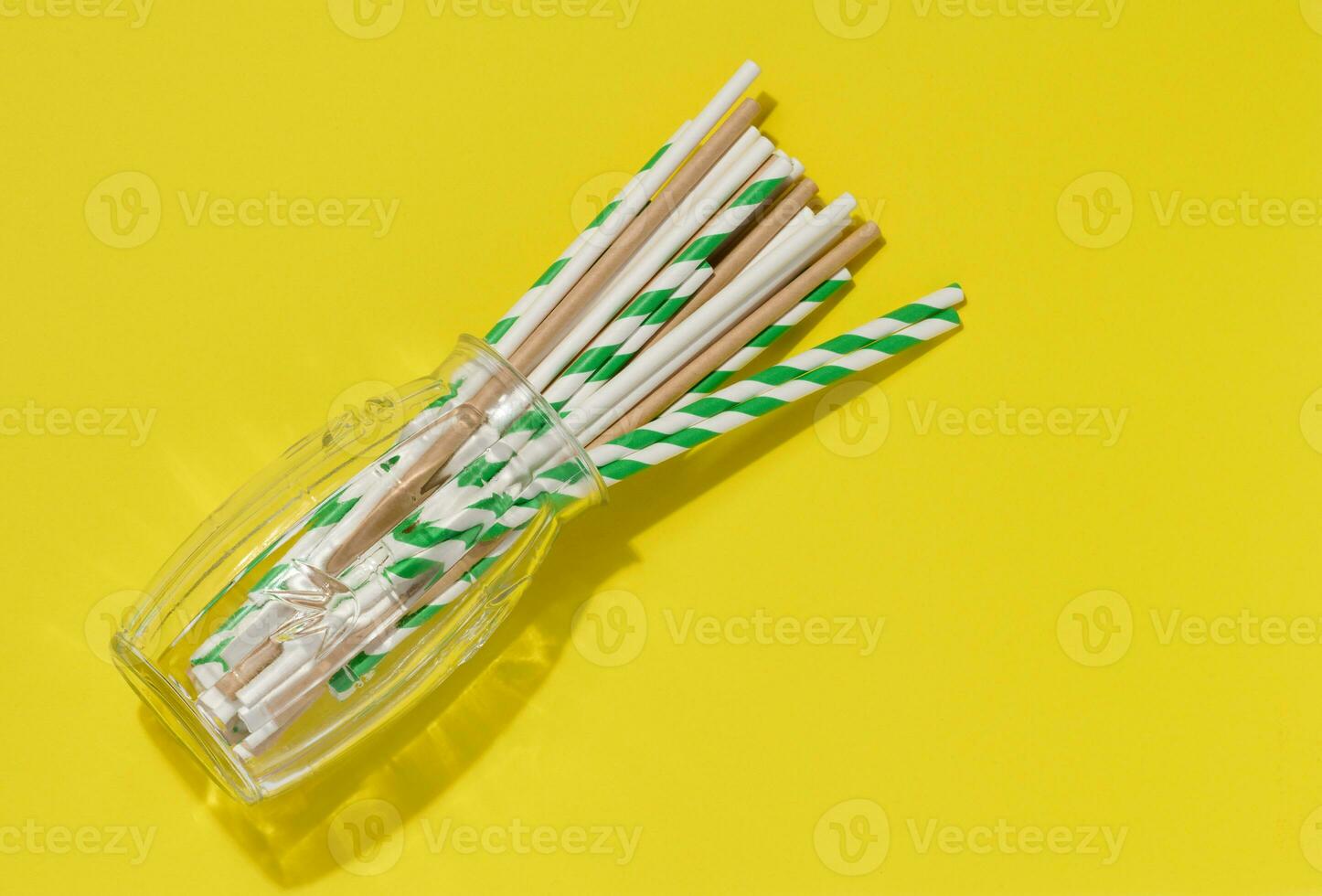 Paper tubes in a transparent glass on a yellow background, top view photo