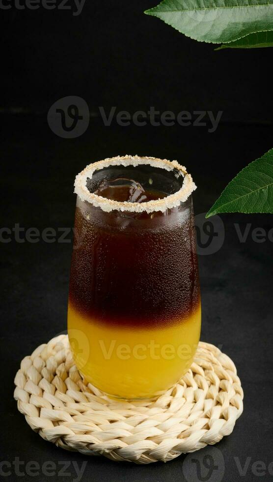 Iced coffee with orange juice in a transparent glass, refreshing bumble coffee on the table, black background photo