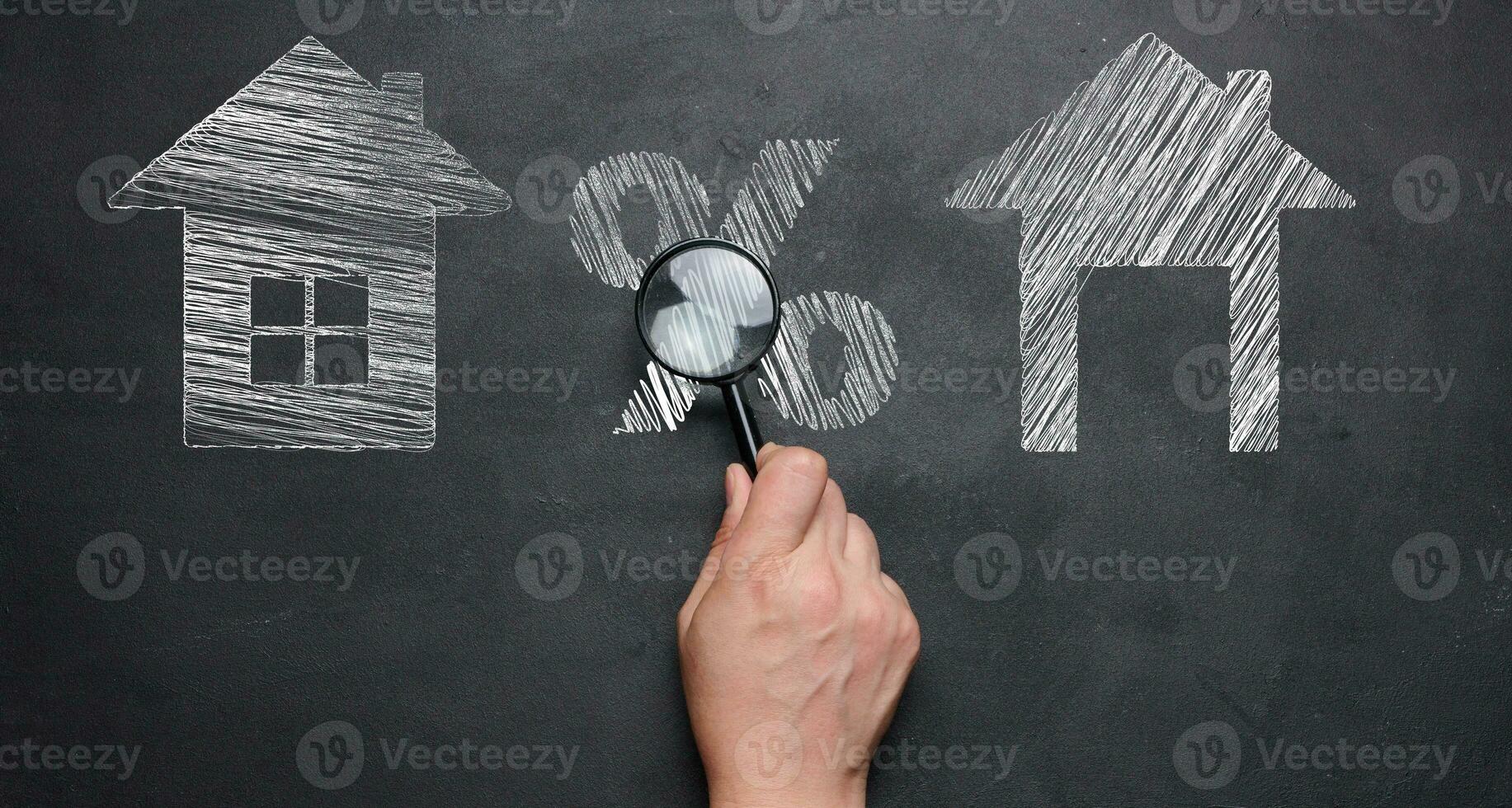 Chalk-drawn houses and a percentage sign on a blackboard, a female hand holding a magnifying glass. Concept of increasing or decreasing mortgage, rent. photo