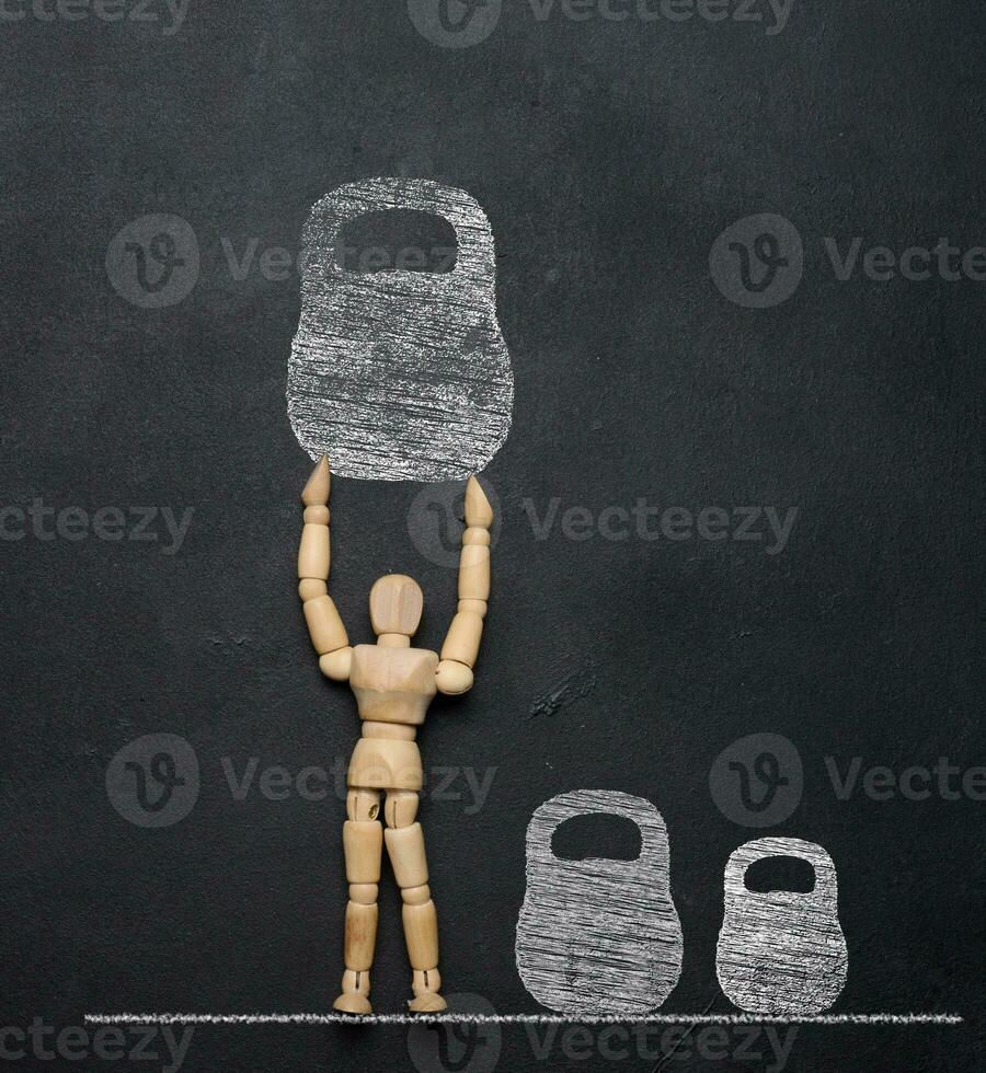 A wooden puppet toy holds a weight drawn on a chalkboard. The concept of a strong personality photo