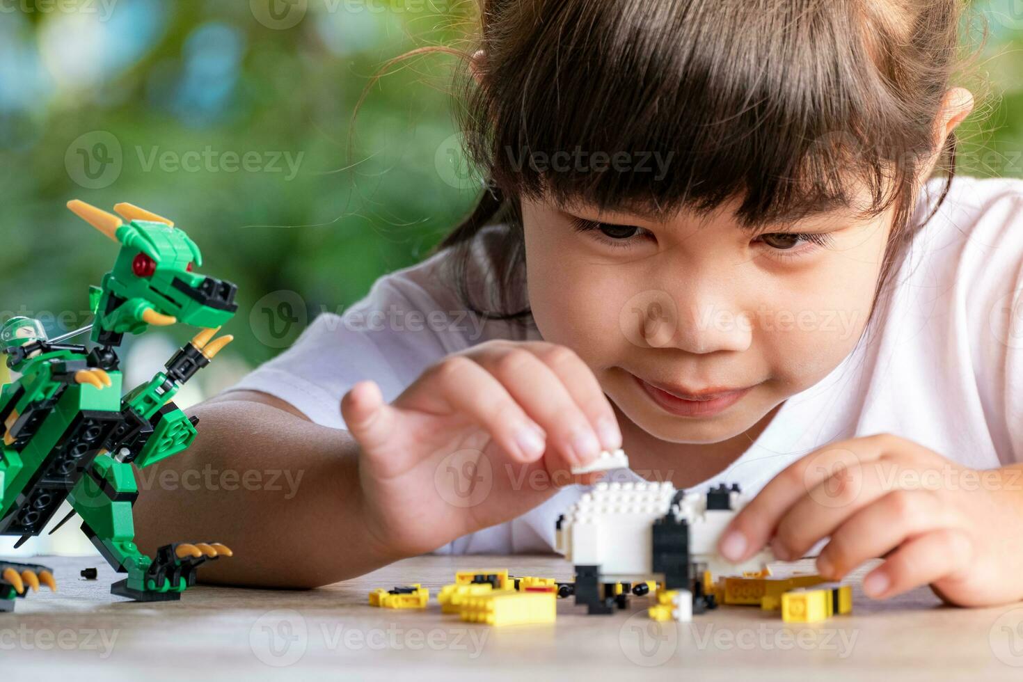 Close up Asian girl 5-6 year old kid playing with Lego bricks or toy at home, Asian girls relax with playing brick blocks on wooden table and enjoy playing toys. photo