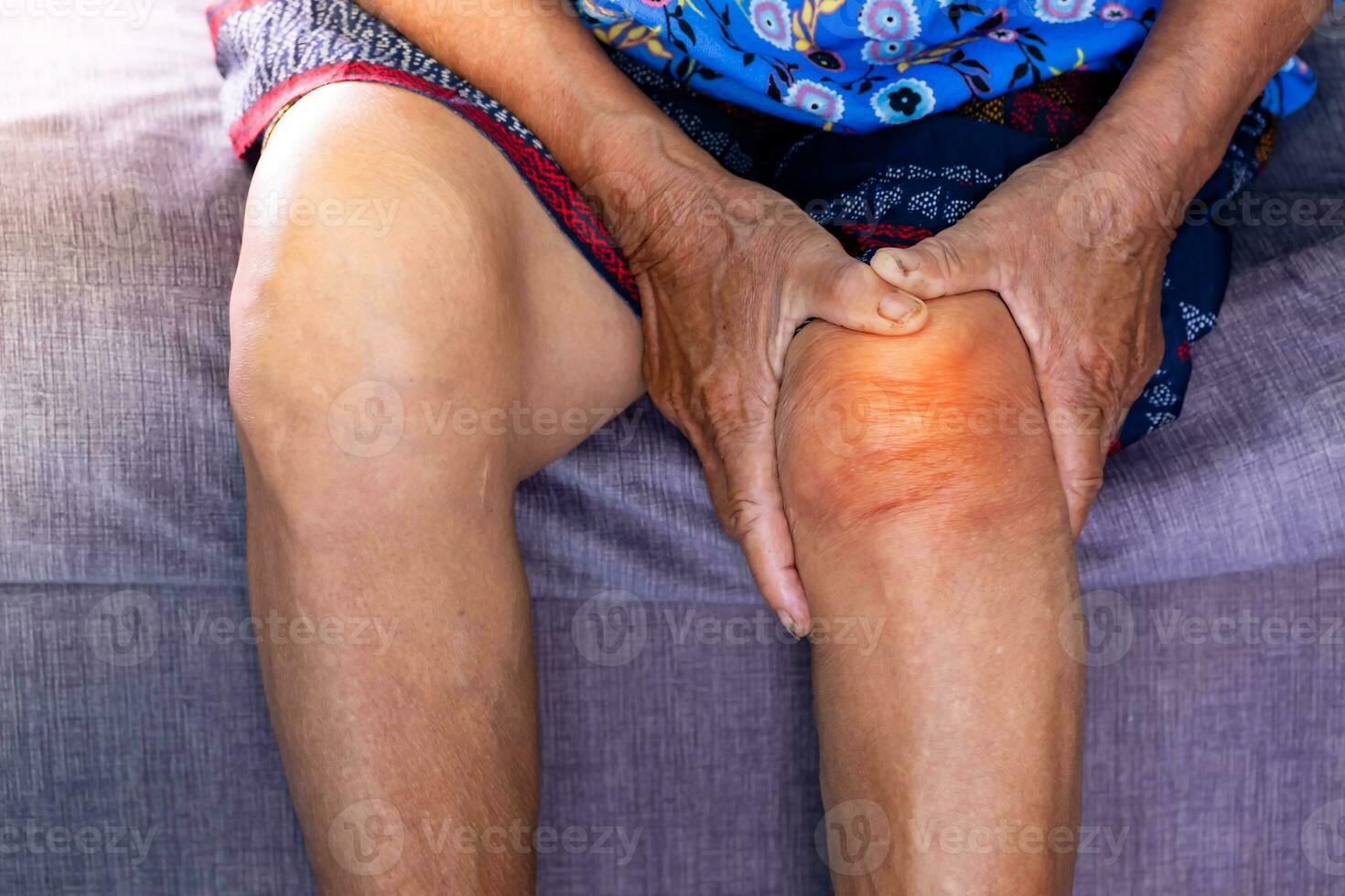 Senior woman holding the knee with pain on sofa in living room at home. Old age. she is having symptoms Pain on both sides of the knee, due to osteoporosis, to retirement age and health care concept. photo