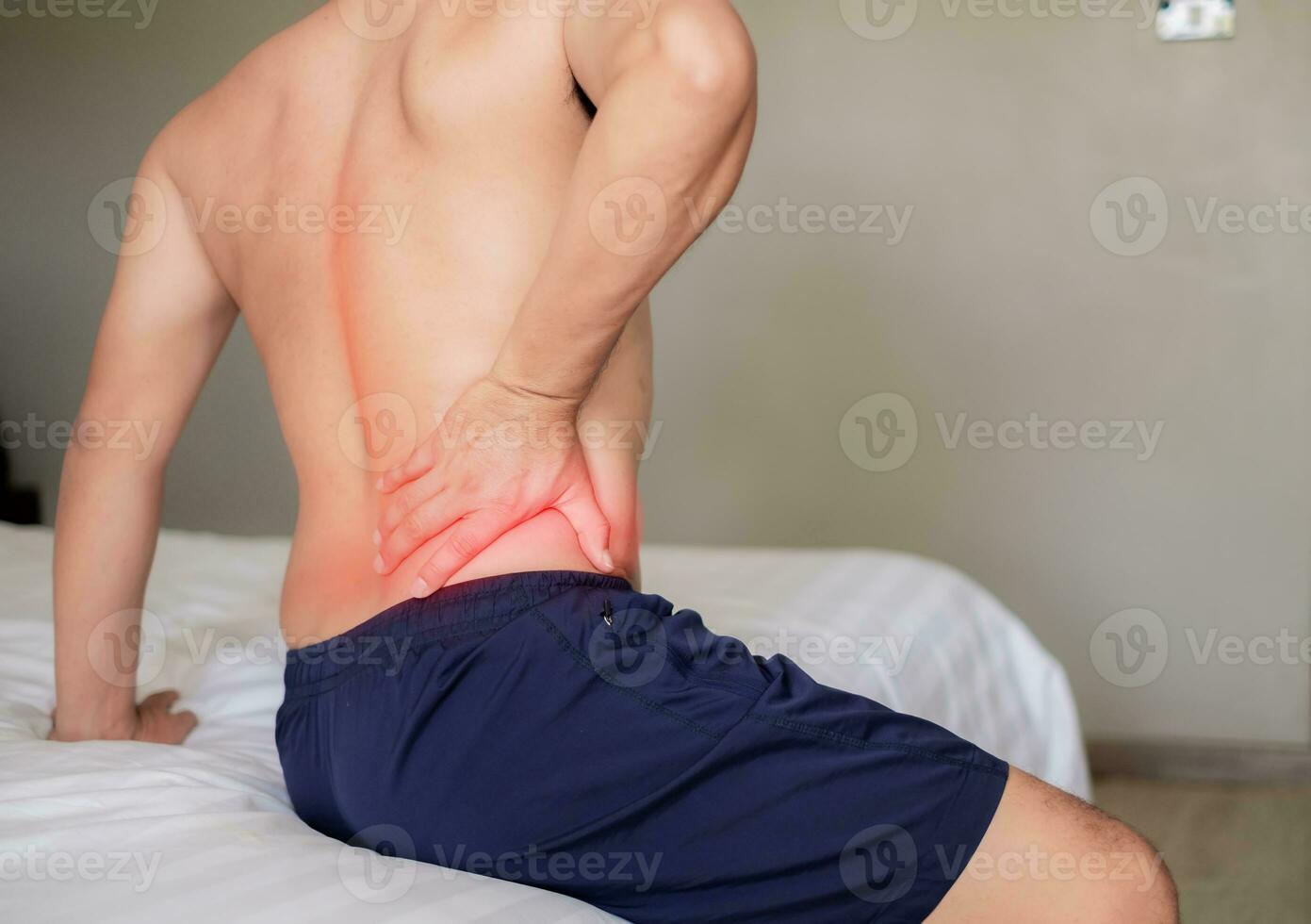 The man sat on the white bed, holding his aching waist as he was about to get up. Inflammation of the lumbar region. Twisting. Getting up in the wrong position. Inflammation of the muscles of the back photo