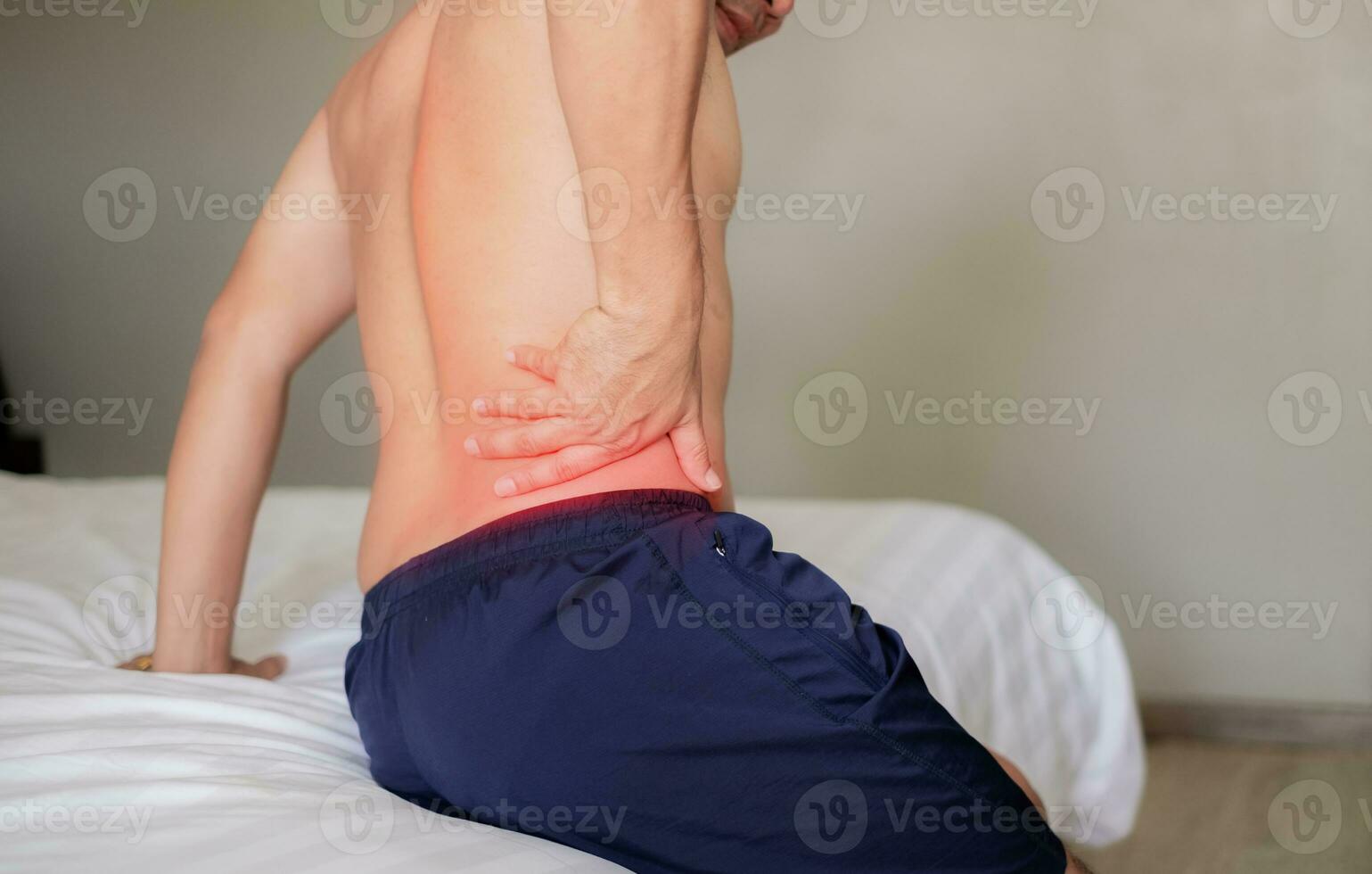 The man sat on the white bed, holding his aching waist as he was about to get up. Inflammation of the lumbar region. Twisting. Getting up in the wrong position. Inflammation of the muscles of the back photo