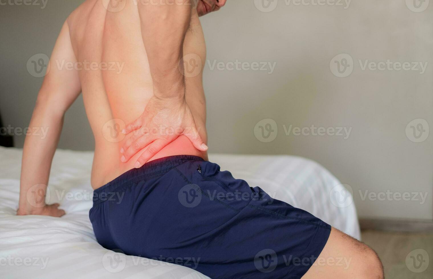 el hombre se sentó en el blanco cama, participación su dolor cintura como él estaba acerca de a obtener arriba. inflamación de el lumbar región. retortijón. consiguiendo arriba en el incorrecto posición. inflamación de el músculos de el espalda foto