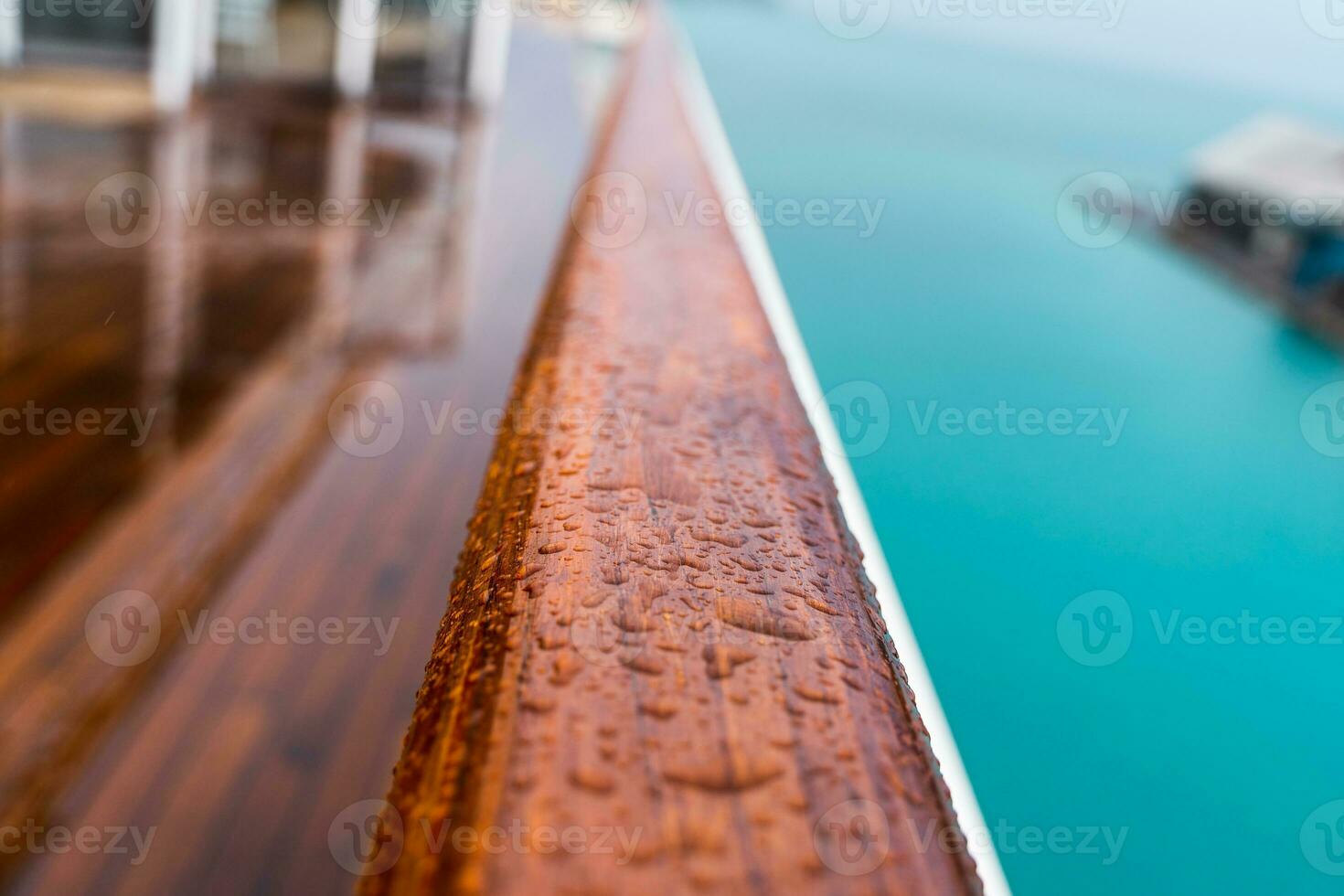 close up of raindrops on a wooden handrail on the deck of a ship photo