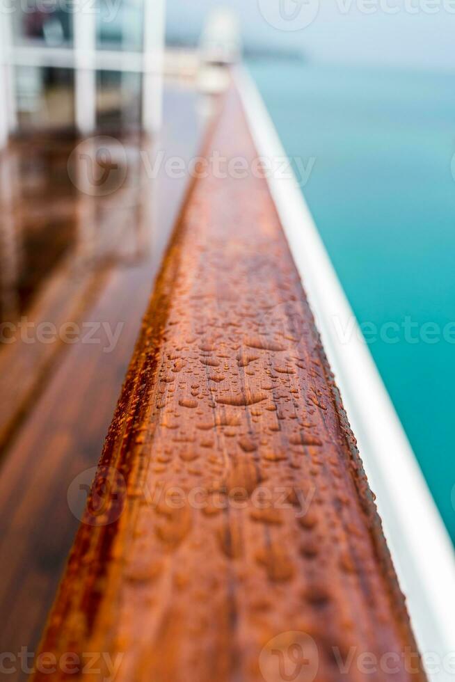 close up of raindrops on a wooden handrail on the deck of a ship photo
