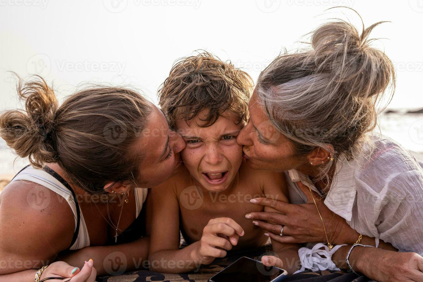 retrato de hermosa medio Envejecido madre y su hija besos el más joven niño en el playa a puesta de sol foto