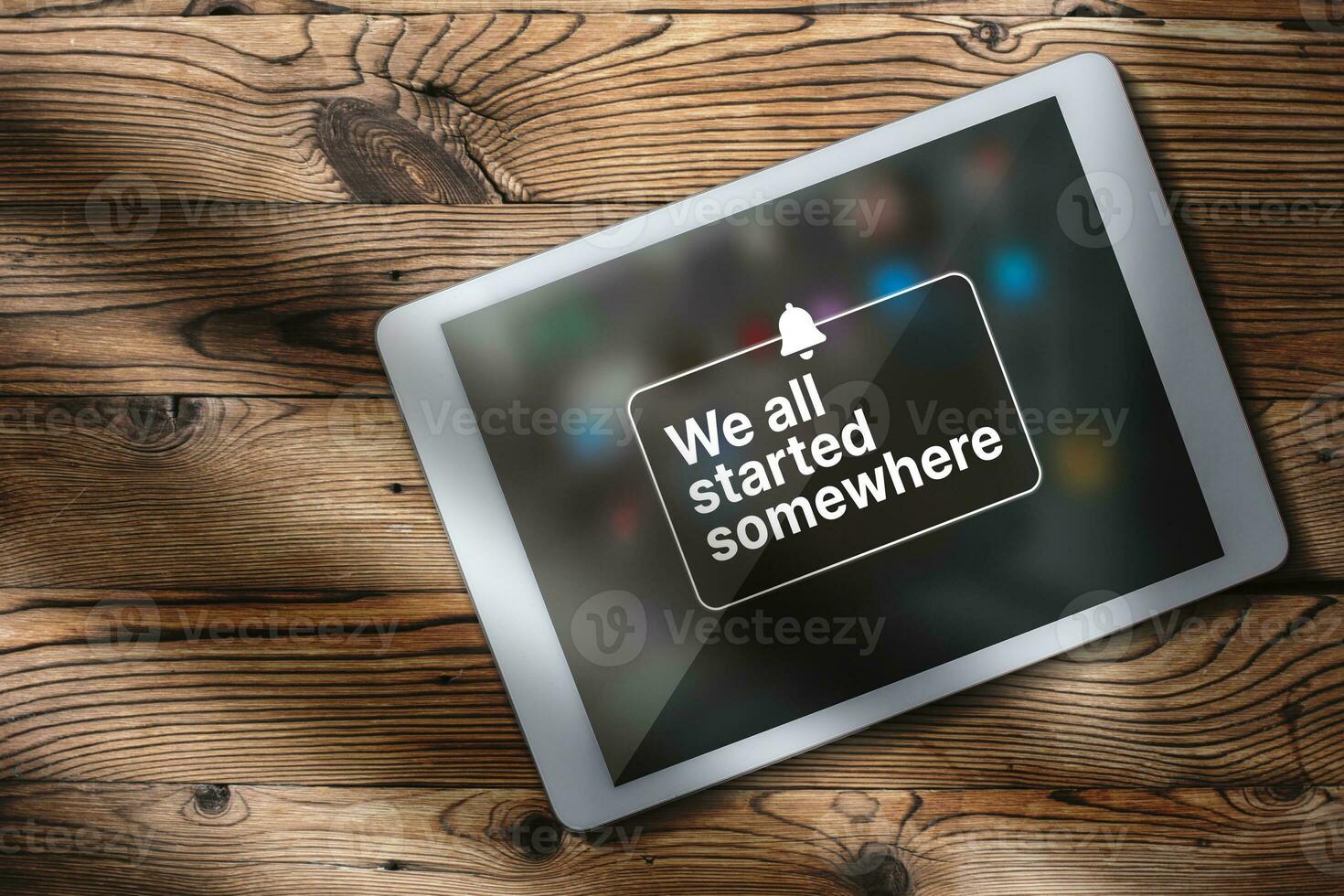 Flat lay photo of digital tablet over wood desk with motivational quote on screen. We all started somewhere quote concept with copy space.