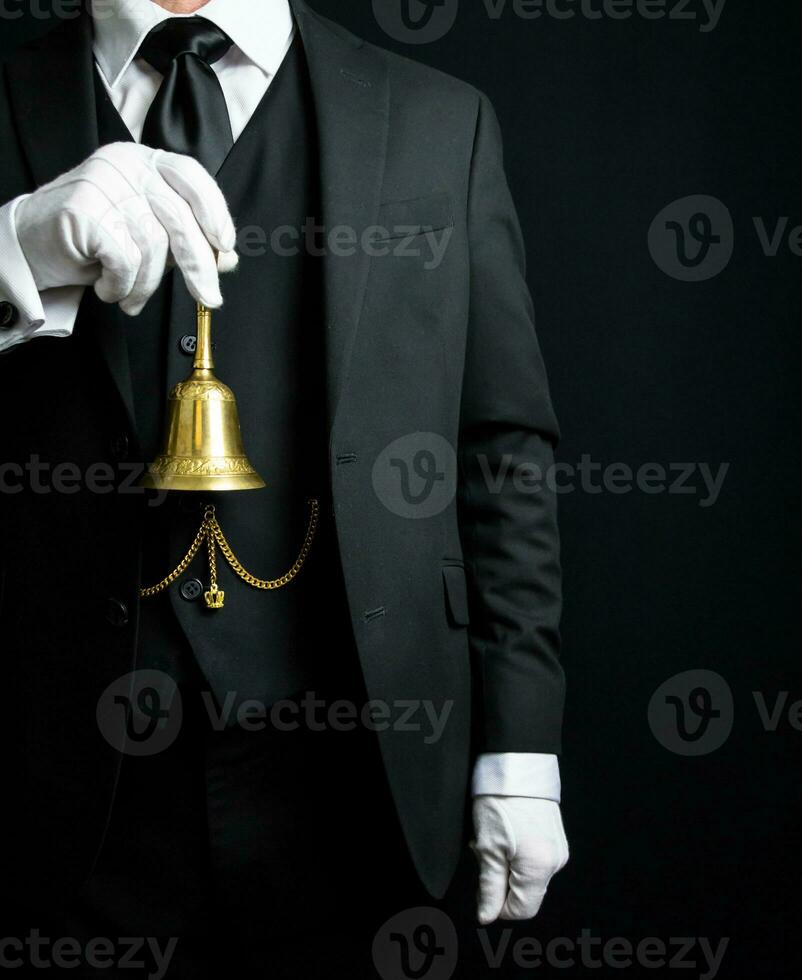 Portrait of Butler or Hotel Concierge in Dark Suit and White Gloves Holding a Gold Bell. Ring for Service Concept. photo