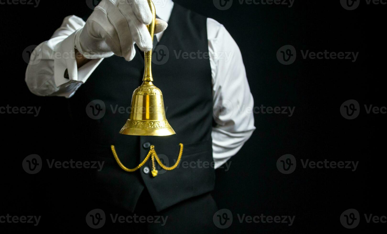 Portrait of Butler or Hotel Concierge Wearing Vest and White Gloves Holding Gold Bell. Ring for Service. photo