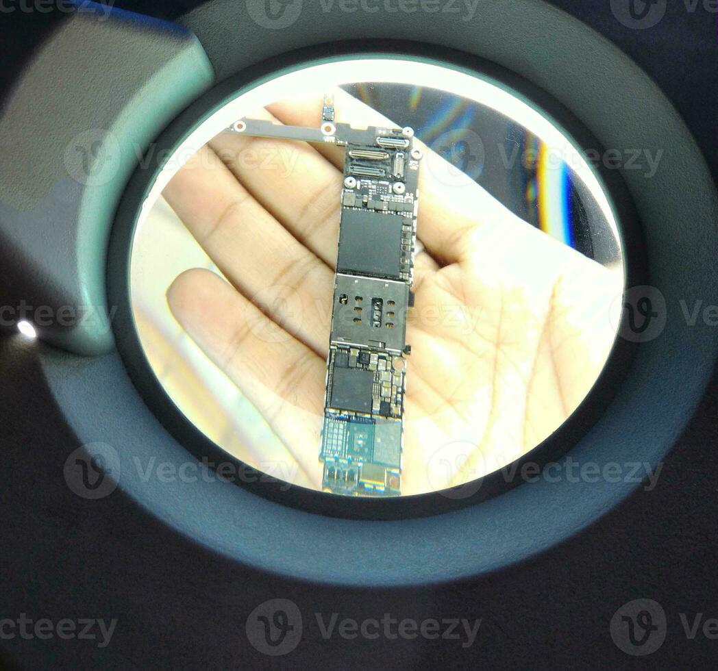 technician using magnifying glass smartphone motherboard photo