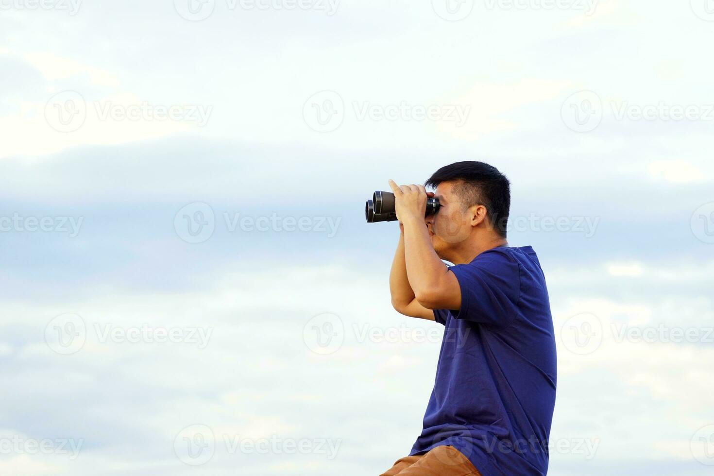 Asian man using binoculars looking nature around mountain campsite with family on vacation. Soft and selective focus. photo