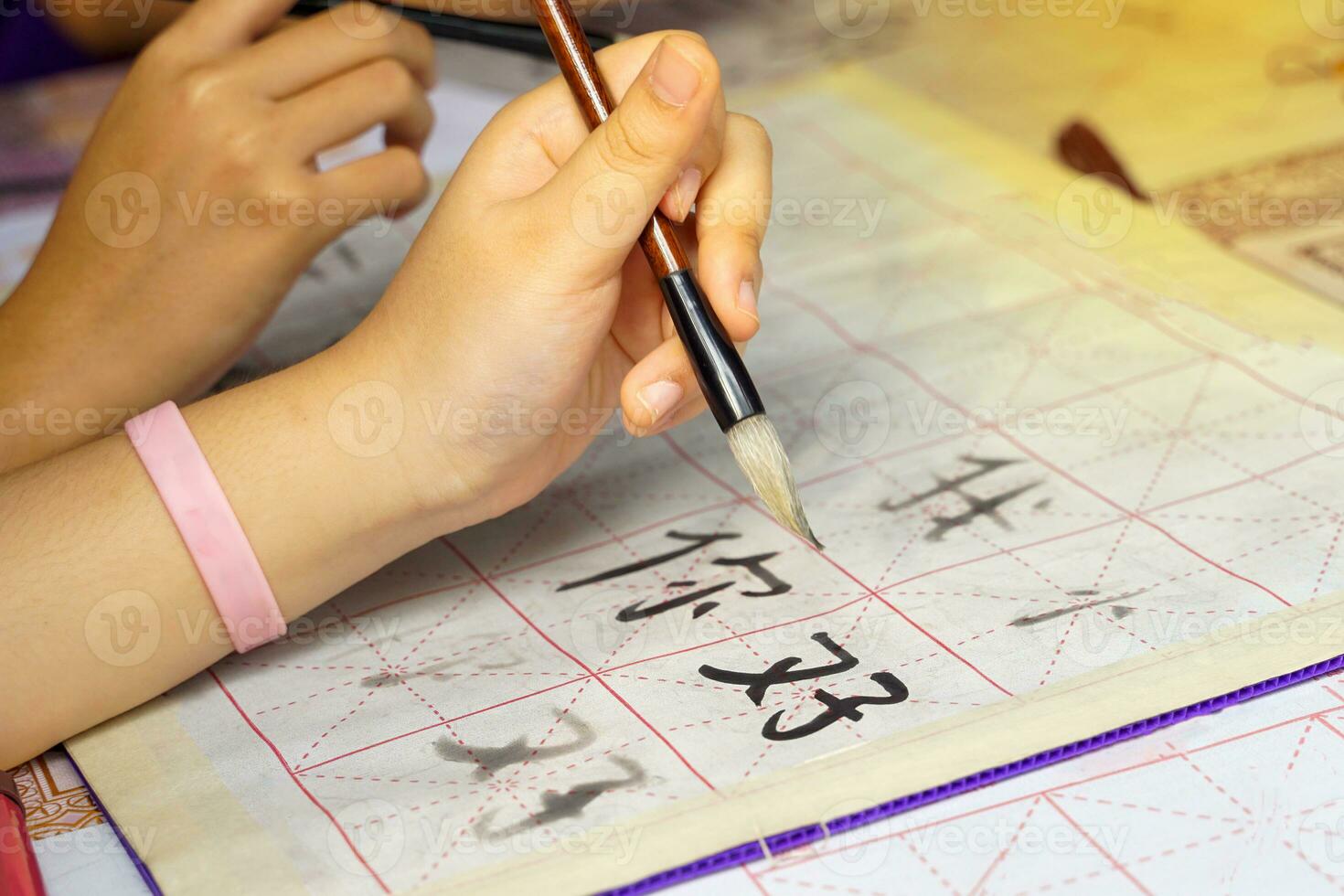 Asian students practice the art of Chinese calligraphy by writing Chinese characters, the word  ni hao , which means hello on paper. Soft and selective focus. photo