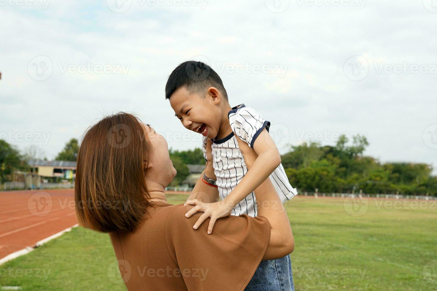 madre participación su hijo arriba el chico sonrió felizmente, teniendo divertida. mientras yendo para un caminar a el cerca estadio en el noche. suave y selectivo enfocar. foto