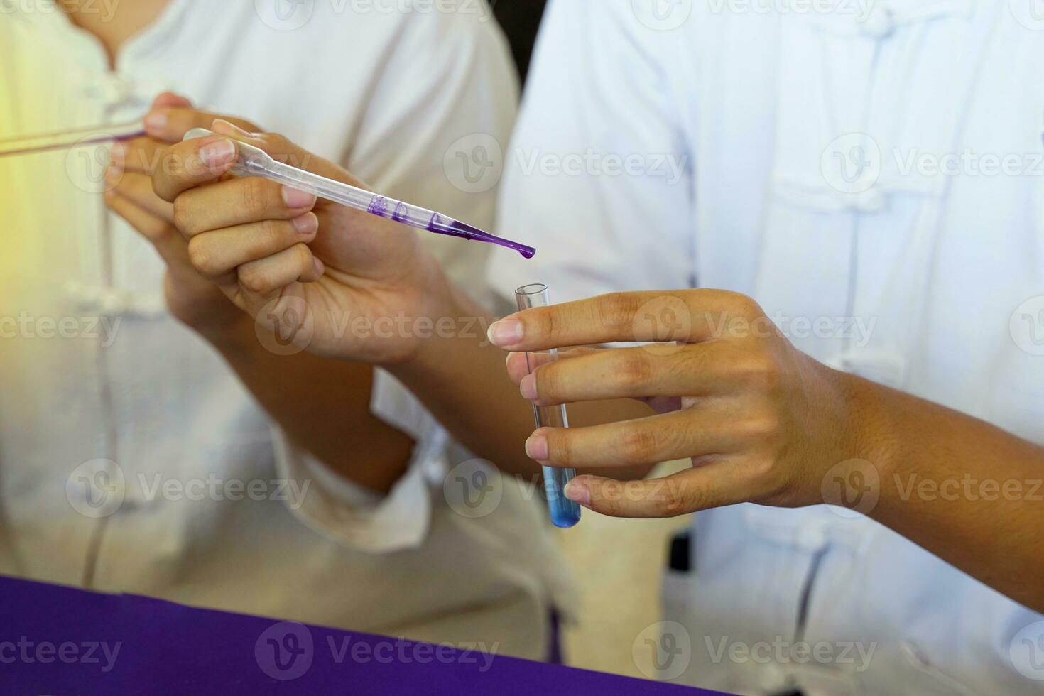Asian students doing science experiments on chemical reactions of substances Students drop a purple solution into a test tube containing a clear solution to change it to blue. photo