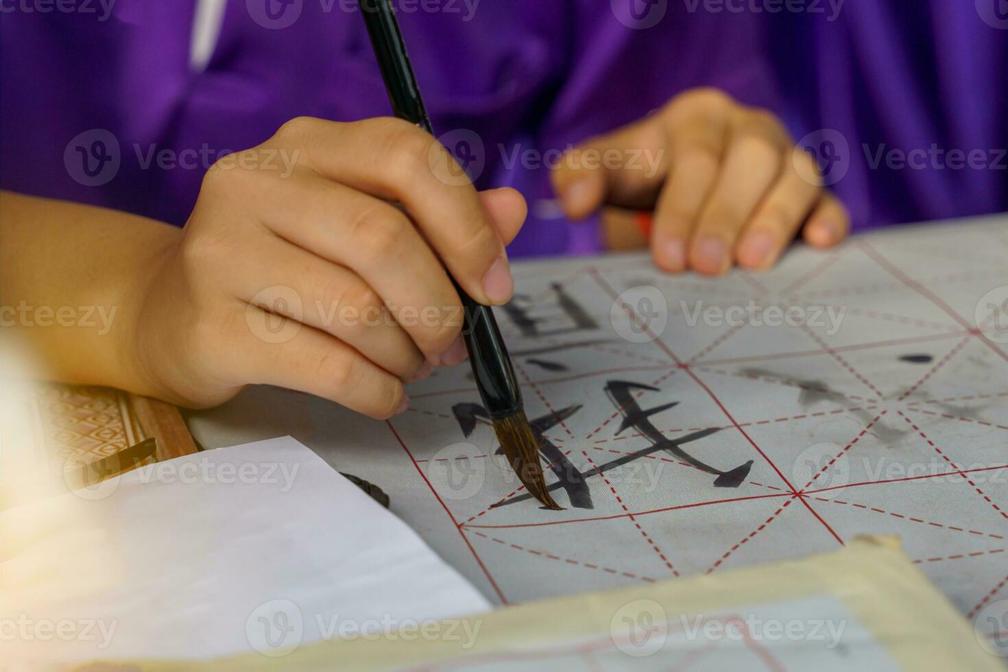 Asian students practice the art of Chinese calligraphy by writing Chinese characters, the word  Wo , which means Me on paper. Soft and selective focus. photo