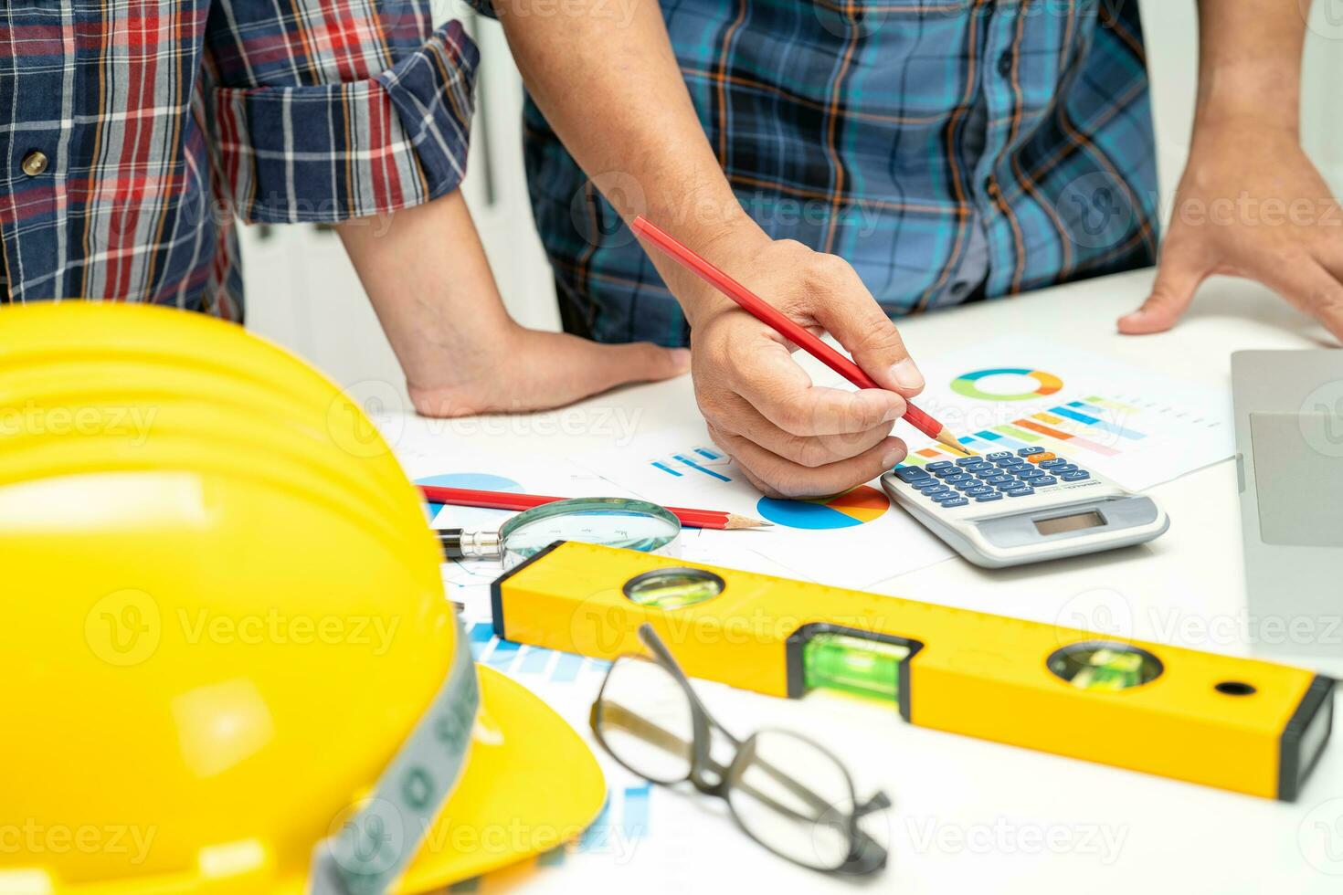 Asian engineer and partner team learn and talk with house plan project blueprint, graph and yellow helmet and engineering construction tools on table work. photo