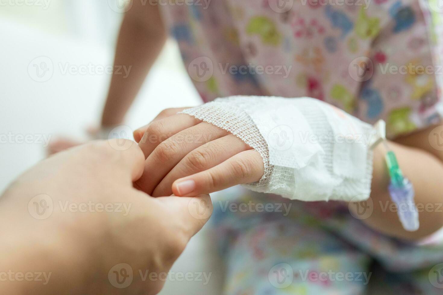 Mother holding child hand with saline IV solution in hospital photo