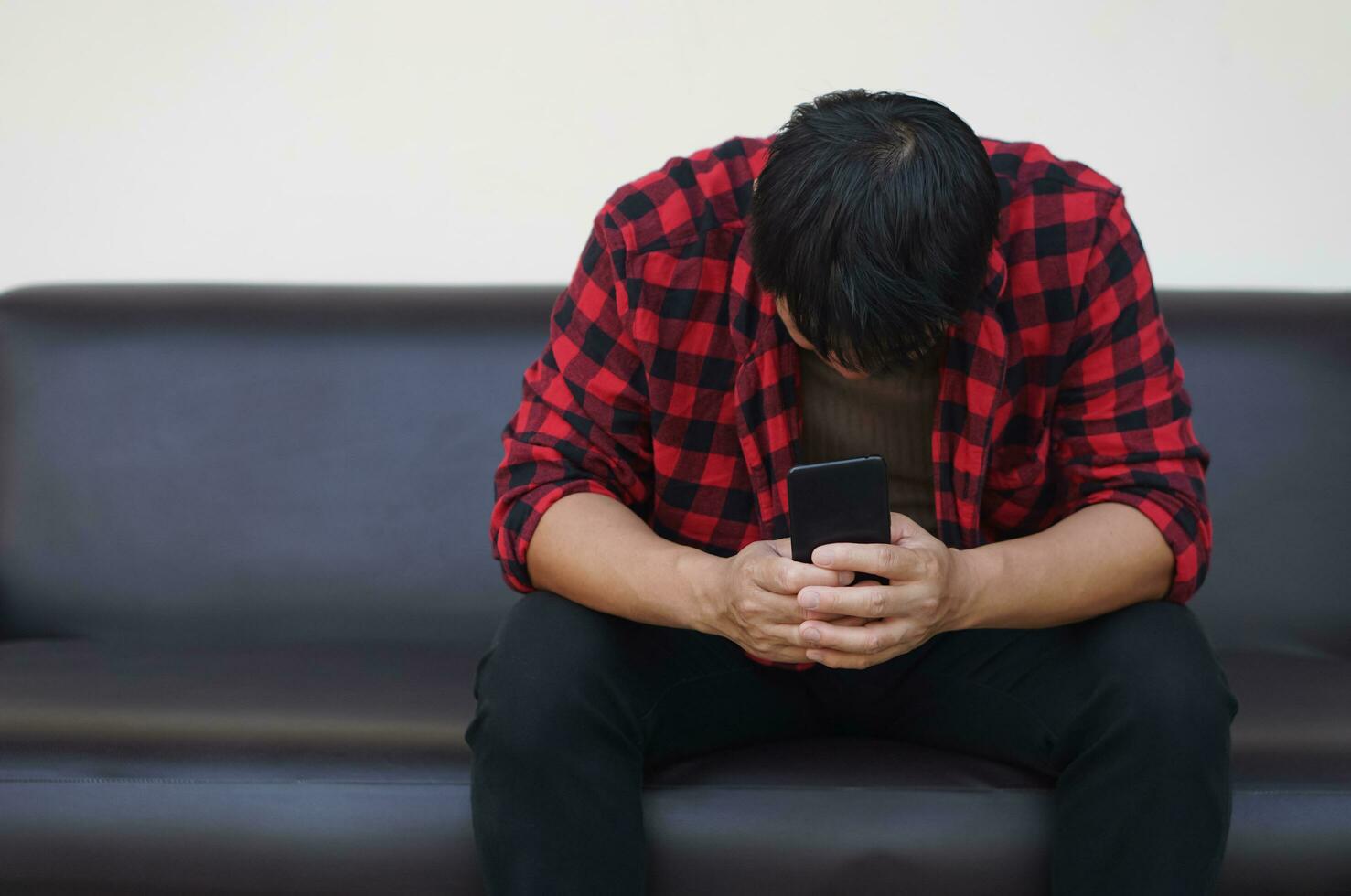 Depressed and unhappy man sits on sofa, face down, holds mobile phone. Concept, know bad news from social media online. Drepression, failure, disappointment, broken heart. guilty,finances crisis. photo