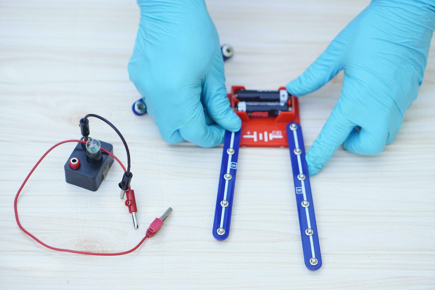 Closeup hands wear blue gloves demonstrate science experiment about electricity circuit. Concept, scientific tools for education, lab lesson. Learning by doing. Teaching aid photo