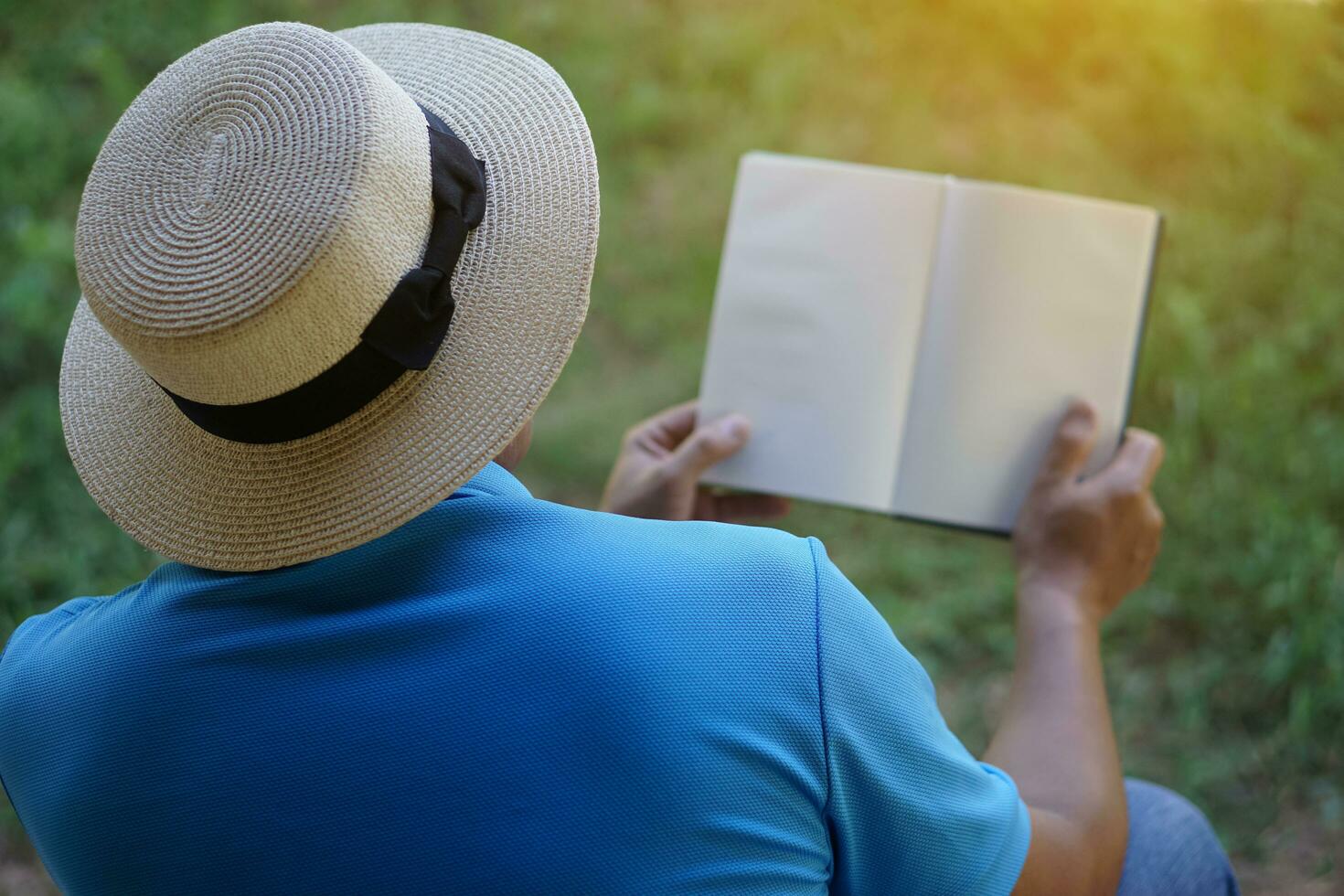 Back view of man wears white hat, blue shirt, open blank page book. Concept. Reading in daily life. Relax time, pastime, hobby. Give time for yourself to read books , magazine, novels. Education. photo
