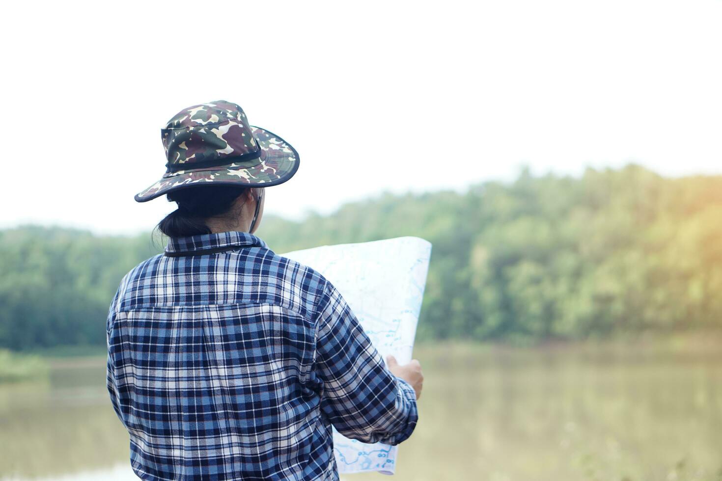 Back view of woman exploror stand beside the lake, holds paper map. Concept, travelling, nature exploration. Ecology study. Pastime activity, lifestyle. Explore environment photo