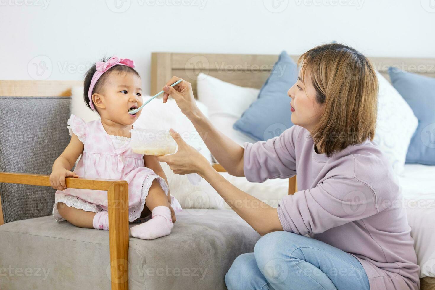 Asian mother is feeding infant formula to her cute toddler baby girl for healthy kid nutrition and motherhood by raising child to grow and parenting concept photo