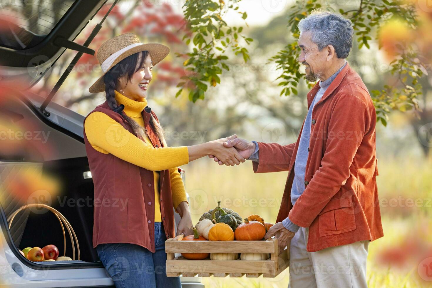 contento granjero familia apretón de manos en orgánicos de cosecha propia Produce cosecha con manzana, squash y calabaza mientras de venta a el coche maletero en local mercado con otoño color desde arce árbol durante otoño temporada foto