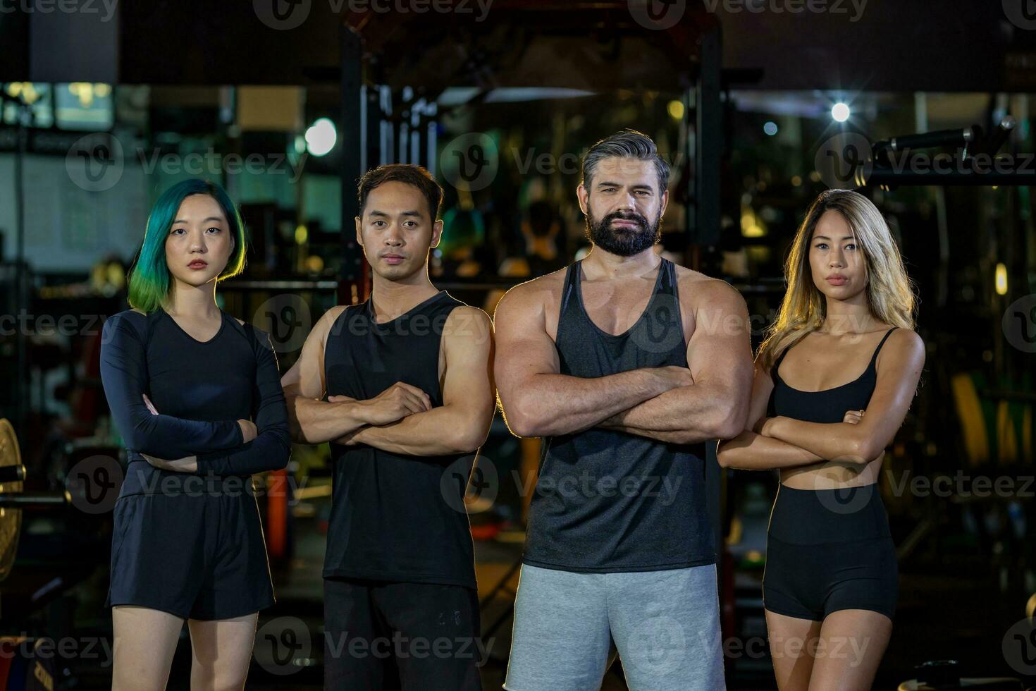 Group portrait of diversity muscular gym trainers standing cross hand together inside gym with dark tone background for exercise and workout concept photo