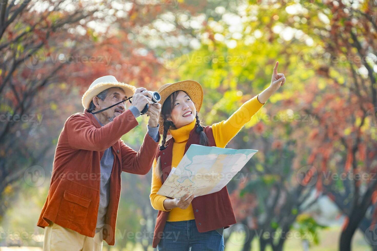 Happy Asian daughter and her senior father are walking together in public park during autumn with maple and ginkgo tree while looking at the map for fall color travel destination and family happiness photo