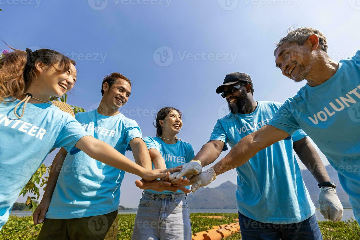 Team of young and diversity volunteer worker group enjoy charitable social work outdoor together in saving environment project wearing blue t-shirt while joining hand in power assemble unity photo