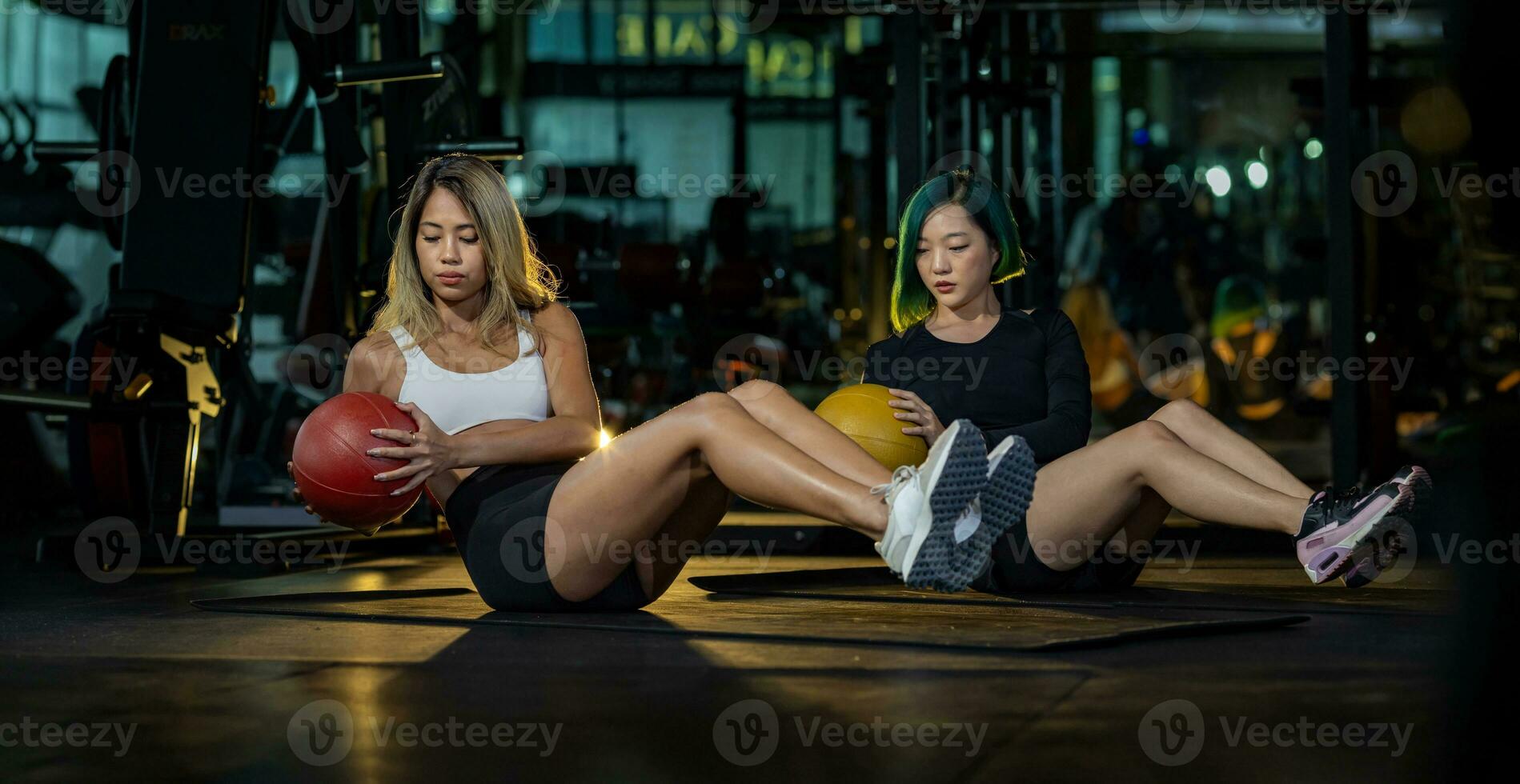 Two Asian women gym partner doing seated oblique twist exercise with weight medicine ball on the floor which strengthen the abs abdominal and core body muscle photo