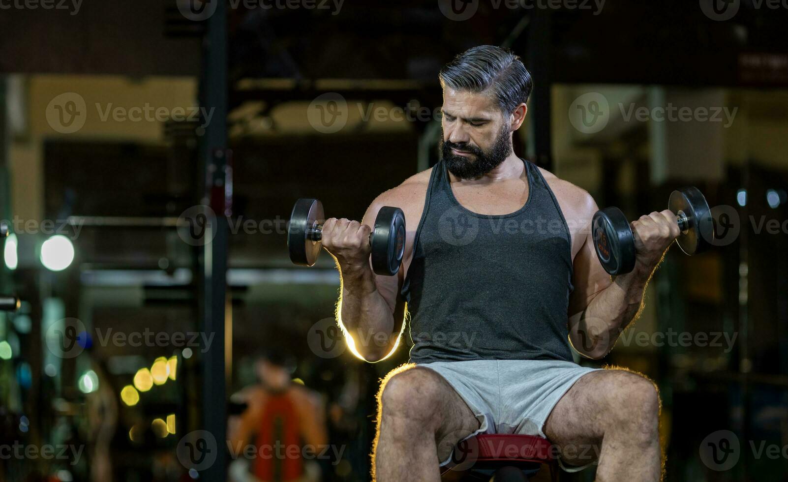 Caucasian beard muscular sport man is practice weight training on double dumbbells for biceps and triceps muscle inside gym with dark background for exercising and workout concept photo