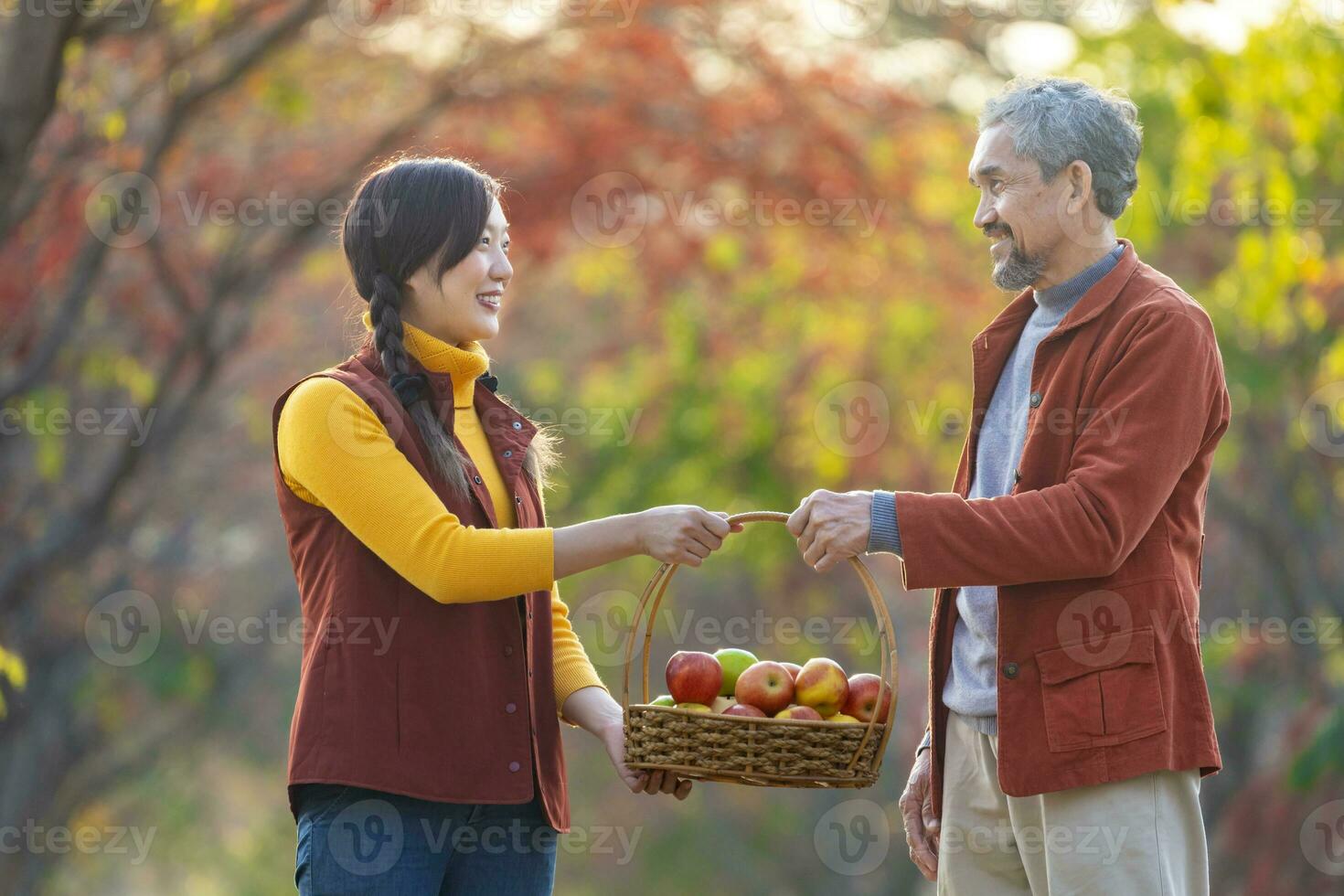 Happy farmer family carrying organics homegrown produce harvest with apple while walking along country road with fall color from maple tree during autumn season photo