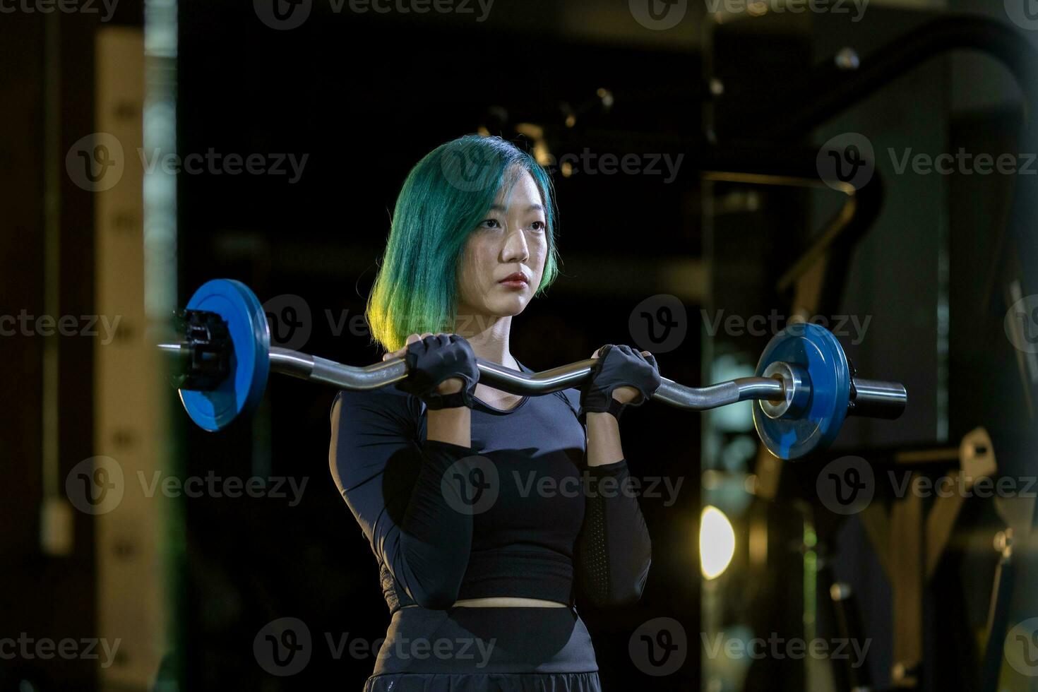 Asian woman is practice weight lifing using easy bar as beginner on barbell for arm and core muscle inside gym with dark background for exercising and workout concept photo