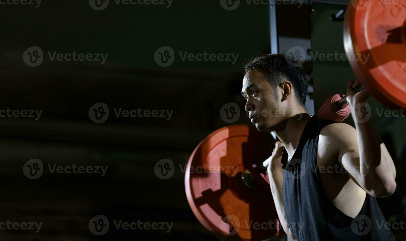Asian muscular sport man is practice weight training on deadlift barbell for core muscle inside gym with dark background for exercising and workout concept photo