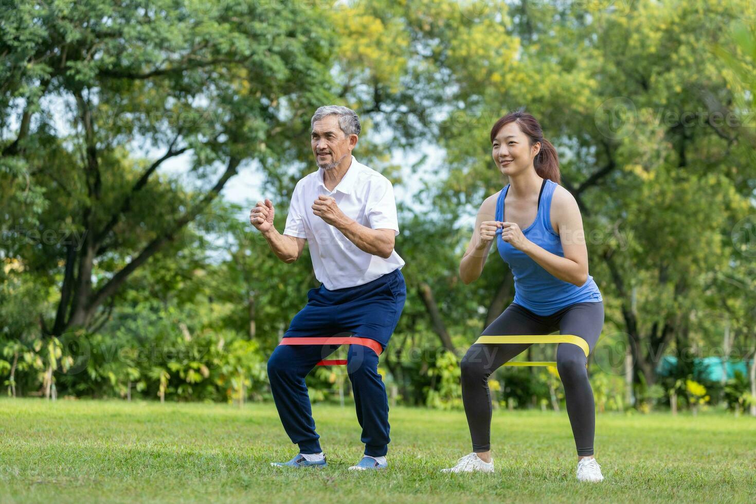 Senior asian man and his daughter are using sport rubber band to build up his leg muscle strength  in the public park for elder longevity exercise and outdoor workout photo