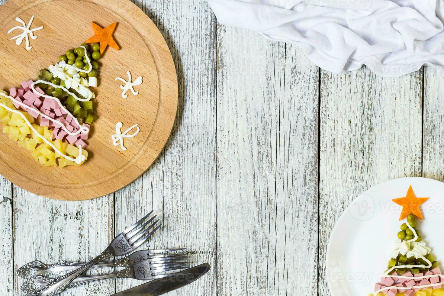 Christmas tree from a salad olivier in plate on a white wooden table. Top view with a copy space photo