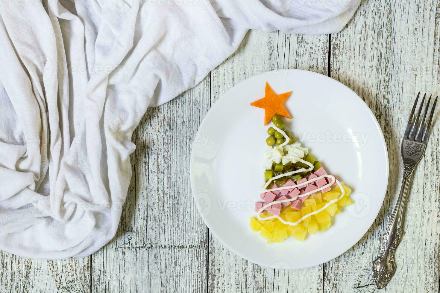 Christmas tree from a salad olivier in plate on a white wooden table. Top view with a copy space photo